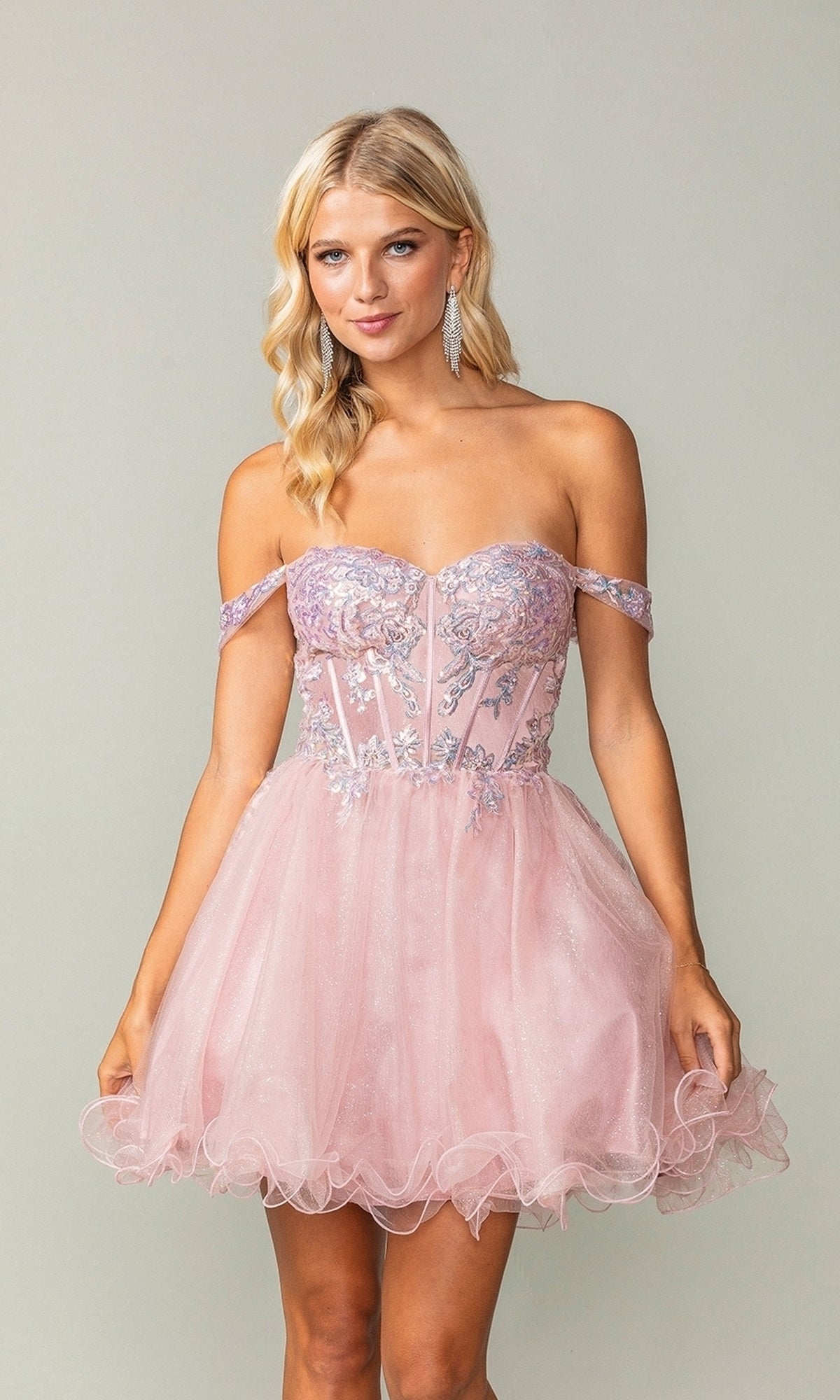 A woman models the Dancing Queen 3383, a short corset homecoming dress with off-the-shoulder sleeves, silver embroidery, a sparkly sheer bodice, and a tulle skirt, posing against a plain background.